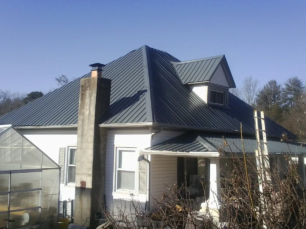 Dark blue standing seam metal roof on a white farmhouse with dormer — Slate & Tile Roof Repair by Roofing Brothers in Savage