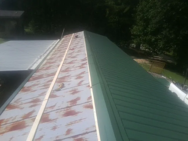 Old rusted panels beside newly installed green metal roofing — Wind Damage Roof Repair by Roofing Brothers in Savage
