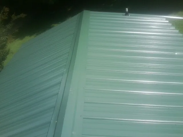New green metal panels meeting at the ridge of a roof — Flat Roof Repair work by our crew in Savage