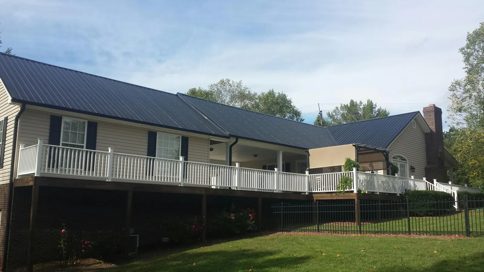 Black metal roof above a long white railed deck on a hillside home in Savage